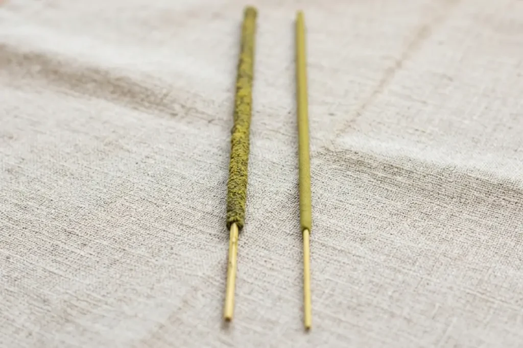 Hand-rolled tulsi incense stick beside a synthetic dipped stick showing quality difference for real herbal incense benefits