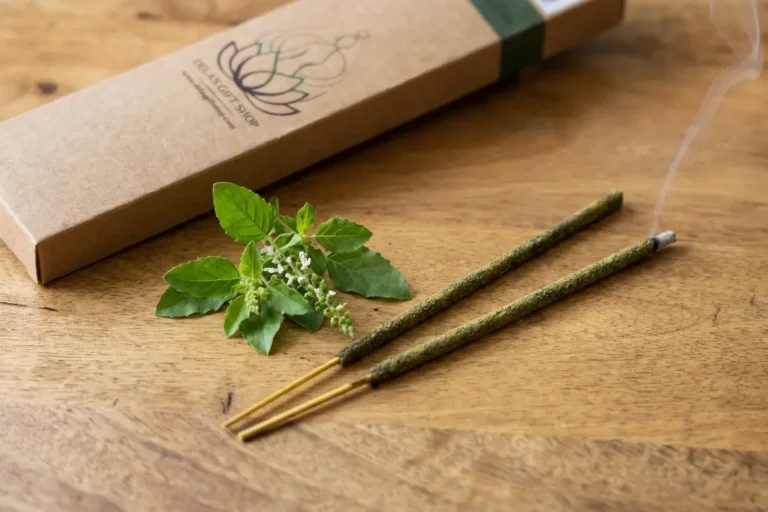 Hand-rolled natural tulsi incense sticks on wooden surface with fresh holy basil leaves and rising smoke
