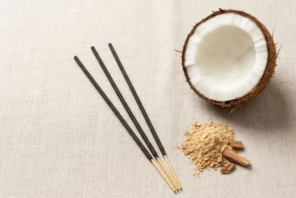 Natural hand-rolled coconut incense sticks UK beside a halved coconut shell and sandalwood powder on a light linen cloth